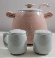 Front view of pink speckled tureen with lid and ladle shown behind matching light blue salt and pepper shakers.