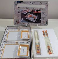 Photo of porcelain sushi plates, dipping dishes, and chopsticks arranged inside the metal box with white foam insert
