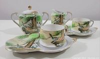 Full view of all 6 pieces including lidded sugar bowl, creamer, two teacups with saucers, and snack plates with peacock designs