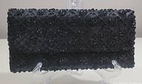 Front view of black bead and sequin embellished clutch on display stand.