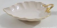 Side perspective of leaf-shaped dish showing white porcelain surface, scalloped edges with gold trim, and sculpted gold handle.