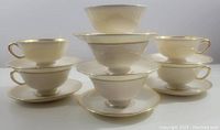 Seven ivory Lenox Tuxedo cups and saucers, stacked and arranged showing gold trim detail.
