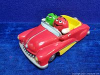 Ceramic collectible figurine showing front and side profile of red and yellow classic car with Red and Green M&M's characters inside.