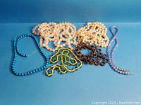 Full lot showing six different strung bead necklaces with various colors including turquoise, cream faux pearls, green faceted, brown, and light blue faceted beads.