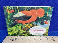 Front cover of the vintage Brooke Bond Tea picture card book titled 'Tropical Birds' showing a large red and black tropical bird in a leafy setting with a measuring scale below.