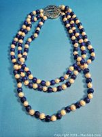 Full view of the triple-strand necklace showing alternating cultured pearls and lapis lazuli beads.