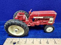 Side view of vintage red Ertl Farmall 404 diecast tractor toy showing length against ruler approx 7 inches, wear to paint visible