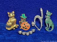 Lot of six cat brooches shown on blue background including gold tone, rhinestone, and enamel designs.