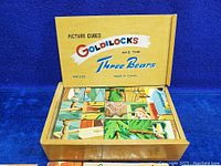 Top view of the wooden box containing the picture cubes with the lid open, showing cubes arranged inside with colorful Goldilocks and the Three Bears illustrations.