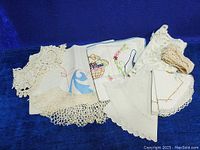 Lot of mixed embroidered and lace linens, various folded pieces on blue backdrop