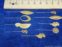 Seven vintage gold tone hat and scarf pins on blue velvet with ruler for size reference