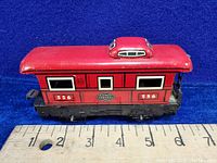 Side view of red Marx New York Central Lines caboose marked 556 on ruler background showing about 4.5 inch length.