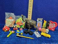 Overview photo showing variety of vintage toys including plastic elephant, small toys, M&M's heart photo frame, toy vehicles, and rubber toys with ruler for scale.