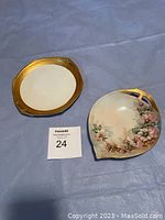 Photo showing two small antique plates on a blue cloth background, the left plate is octagonal with gold border, the right plate a floral design with curved edges.