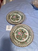 Pair of round hand-painted antique Chinese porcelain plates on blue fabric background showing detailed floral designs and geometric borders.