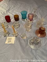 Photo showing various clear and colored glass candle holders arranged on a fabric surface.