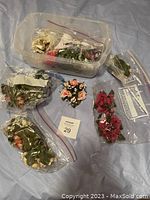 Photo showing miscellaneous flower candle rings in plastic bags and container, various colors and styles.