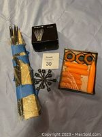 Two bundled Scandinavian style black metal candle holders, an open box of eight orange taper candles, a black box labeled HJERTE containing pins or spikes, and a box with four large black hexagonal wax candle holders with more orange candles