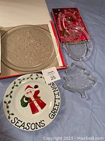 Photo showing four holiday dishes: beige embossed glass plate, red and clear glass divided tray, Santa Claus ceramic plate, and Christmas tree-shaped glass plate.