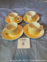 Four bright yellow striped cups placed on matching yellow and white saucers laid out on a fabric surface.
