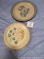 Photo of two serving plates: one metal Pfalzgraff approx 12 inches diameter with gray floral pattern, and one ceramic stoneware approx 11 inches diameter with colorful flowers and yellow rim.