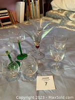 Four pairs of stem glasses displayed on fabric surface, largest pair with red heart inside stem clearly visible. Other pairs have green stems and small gold accents.