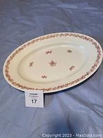 Oval antique turkey platter with small pink rose floral pattern on white base, photographed on blue fabric background with auction lot card