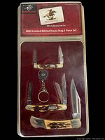 Top view of 2003 Limited Edition Winchester Ersatz Stag 3 Piece Set including three knives in collector's gift tin with red velvet background and Winchester branding.