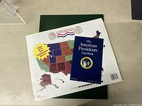Green album folder laid flat with the American Presidents Fact Booklet on top and a USA map design on the inside showing slots for quarters of all 50 states.