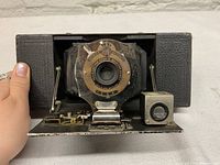 Front view of Kodak Brownie Camera with lens, fold-out bellows, and front metal plate with branding and model information.
