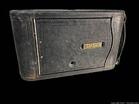 Front view showing black leather casing and brass nameplate on camera.