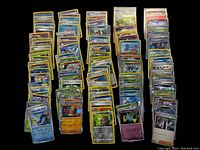 Top-down view of over 100 sleeved holographic Pokémon cards arranged in neat columns showing a variety of types and characters.