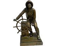 Front angled view of the bronze statue showing the man steering the wheel on a detailed base.