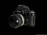 Three-quarter view of Nikon F camera body with attached lens against black background