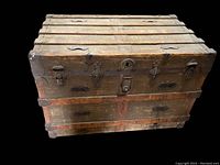 Front view of the wooden trunk showing metal straps, locking mechanism, and handles