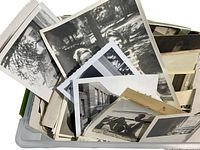 A container filled with a tightly packed stack of black and white vintage photographs showing various outdoor scenes and portraits.