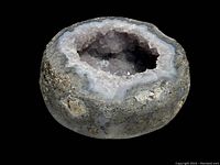 White crystal geode with natural rough stone exterior and hollow interior filled with crystals, shown from angle to display size and form.