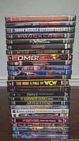 Stack of 25 WWE DVDs showing spines with titles of wrestling DVDs and biographies.