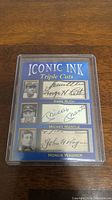 Blue Iconic Ink Triple Cuts collectible card with Babe Ruth, Mickey Mantle, Honus Wagner autograph facsimiles in protective plastic case on wooden surface.