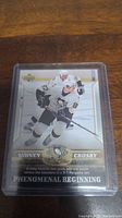 Front of Sidney Crosby rookie hockey card in protective case showing player in Penguins uniform, card number 87, with 'Phenomenal Beginning' text and Upper Deck logo.