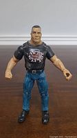 Front view of The Rock action figure wearing black graphic T-shirt and blue pants.