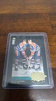Photo of a 1990-91 Upper Deck hockey card featuring Wayne Gretzky and another Edmonton Oilers player in their team uniforms on ice.