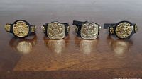 Four miniature WWE Championship belts lined up on a wooden surface, showing front designs