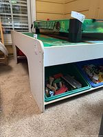 Full side view of the white activity table showing bins filled with toy pieces underneath and air hockey game on top.