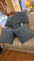 Six blue throw pillows arranged on a white couch in a living space showing size and color.