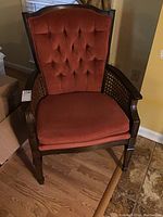 Front view of rust-colored upholstered chair with tufted back and rattan weave arm sides, showing overall design and condition.