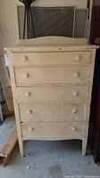 Front view of the vintage cream-colored wooden chest with five drawers, showing paint chipping and crackled top.