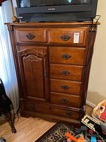 Front view of Stanley chest of drawers showing six drawers, one door with decorative handle and carving details, and a TV on top (TV not included).