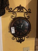 Full frontal image of the metal wall clock showing dial, hands, and the decorative scrollwork frame.