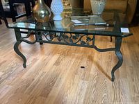 Front angle view of the glass top and wrought iron base showing the ornate scrollwork and curved legs.